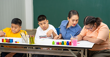 Teacher sitting with three students while they paint.