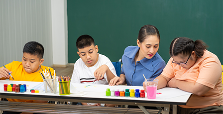 Teacher sitting with three students while they paint.