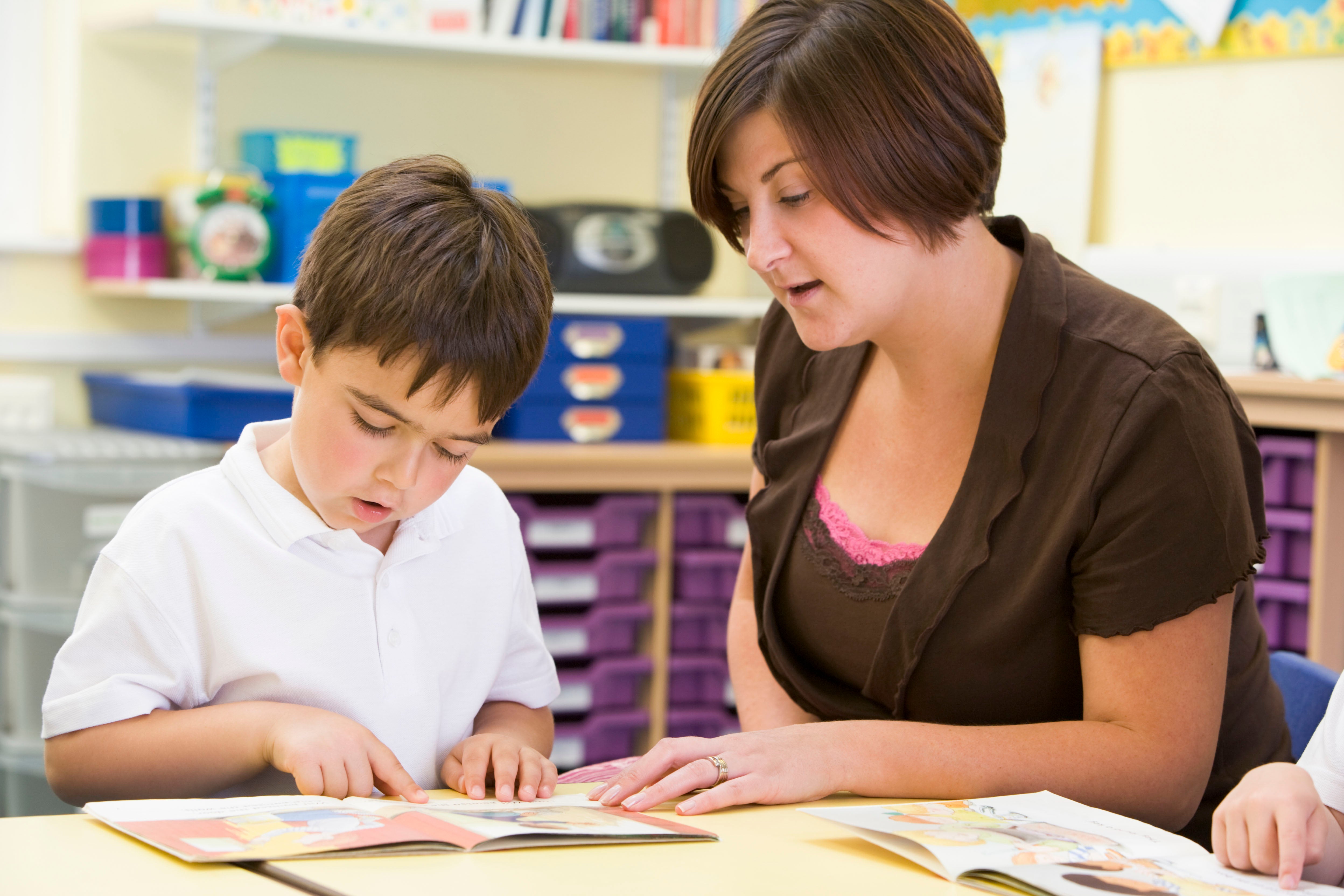 Teacher and student sitting a desk while reading a book together.