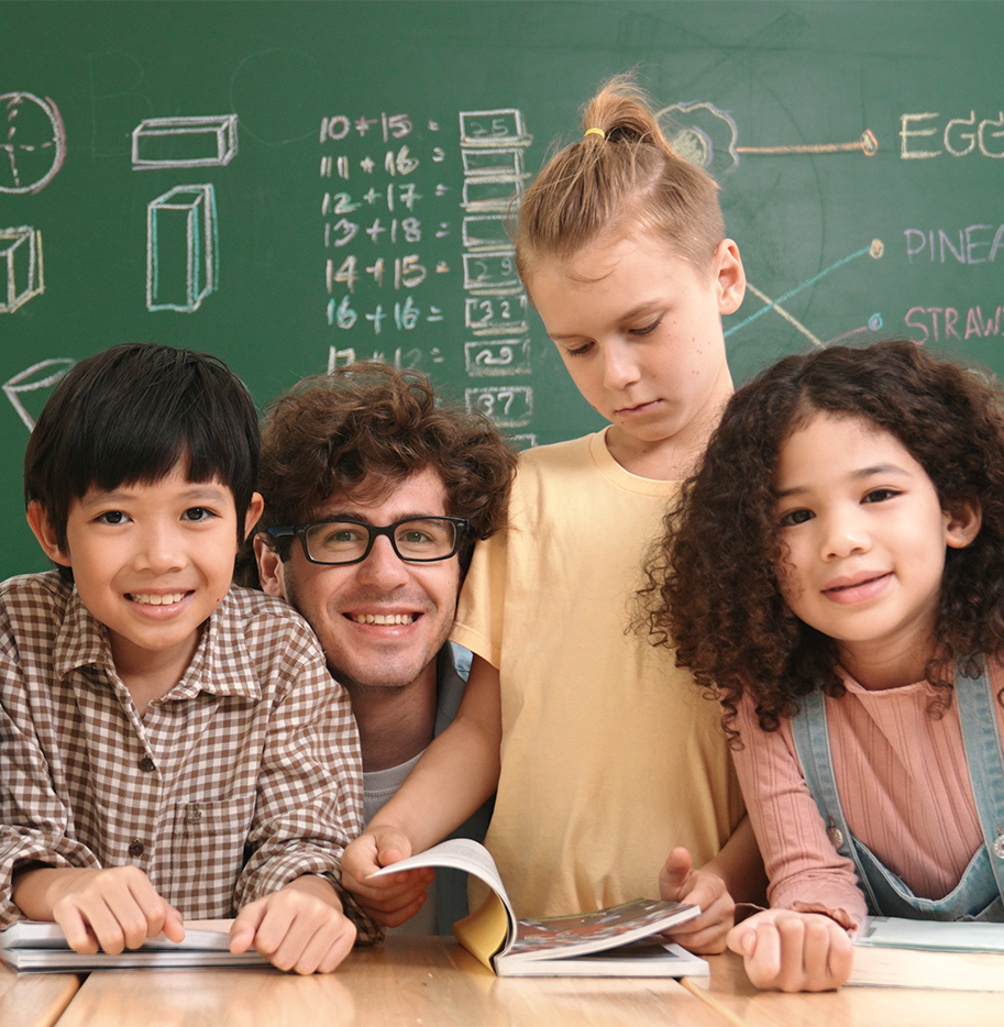 Teacher sitting at his desk with students on either side of him.