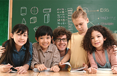 Teacher sitting at his desk with two students on either side of him.