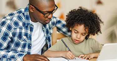A teacher sitting with a student that is practicing writing.