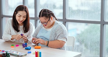 Women sitting with student working on forming shapes out of clay.