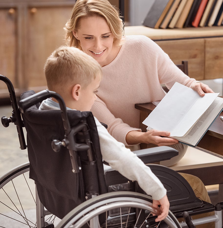 Boy in wheelchair working with teacher who is holding a book for him.