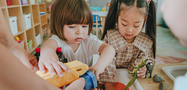 Two children in a classroom getting toys from a bin