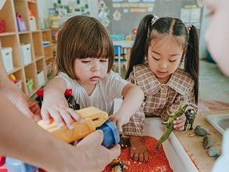 Two children in a classroom getting toys from a bin